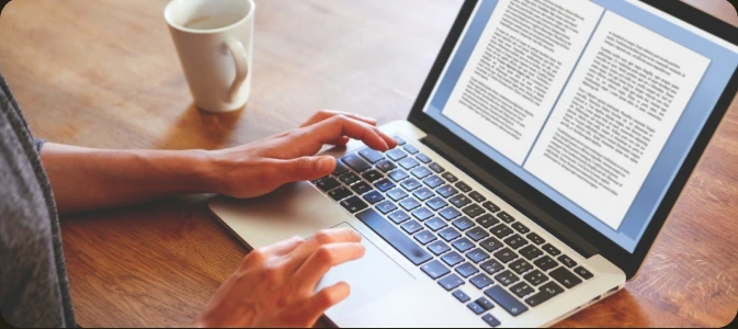 A writer reviewing a manuscript on a laptop beside a cup of coffee